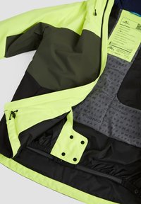 Veste jaune et noire haute visibilité avec fermeture éclair, étiquette intérieure affichant la marque et les détails du tissu, et bouton pression réglable à l'ourlet.