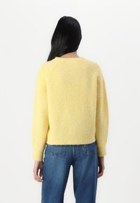 Pull en tricot jaune avec une finition douce et texturée, des manches raglan et une taille courte, assorti à un jean en denim bleu.