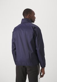 Marine letvægtsjakke med høj krave, elastiske manchetter og en kant. Glat tekstur, minimalistisk design og ingen synlige elementer eller mønstre.