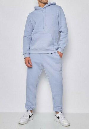 Ensemble de sweat-shirt à capuche et de pantalon de jogging bleu clair en tissu doux, avec une poche avant, une capuche à cordon de serrage et des poignets côtelés, associé à des baskets blanches.