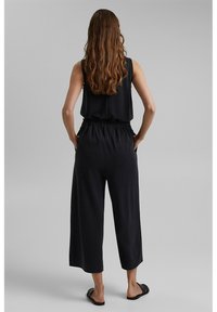 Combinaison noire à manches sans manches, taille élastique, et pantalon à jambes larges. Tissu lisse avec une coupe décontractée et sans motifs.