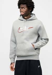 Γκρι φούτερ με κουκούλα, μπροστινή τσέπη,  κορδόνι στην κουκούλα και λευκό λογότυπο Nike σε καλλιγραφικό στυλ. Διαθέτει ριμπ μανσέτες και τελείωμα, συνδυασμένο με μαύρο παντελόνι.