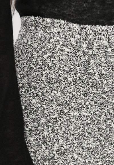Țesătură texturată gri și albă cu un model pătat, având un tricot gros și moale. Materialul negru este vizibil deasupra, creând un contrast.