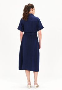 Vestido de lino azul marino con mangas cortas, cintura ceñida y falda hasta la rodilla. Presenta un cuello y detalles de botones en las mangas.
