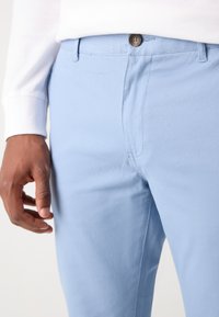 Helle blaue Baumwollhosen mit glatter Textur, mit einem Knopfverschluss, seitlichen Taschen und einem schlanken Schnitt.