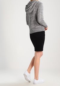 Felpa grigia lavorata a maglia con cappuccio e coulisse, indossata sopra pantaloni corti neri e sneakers bianche. Il materiale è morbido, con una finitura testurizzata.
