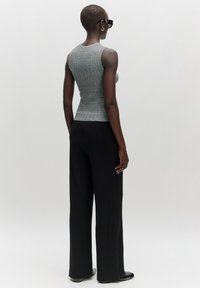 Graues, gestricktes Tanktop mit einer figurbetonten Silhouette, kombiniert mit hochgeschnittenen schwarzen, weit geschnittenen Hosen, die Textur und Kontrast betonen.
