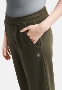 Olijfgroene joggers met een relaxte pasvorm, elastische tailleband, zijvakjes en een subtiele logo-detail in grijs op de linker dij.