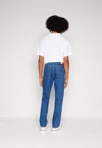 Vaqueros azules de mezclilla con corte recto, que cuentan con bolsillos traseros. Llevados con una camiseta blanca lisa y zapatillas blancas con suela gruesa.