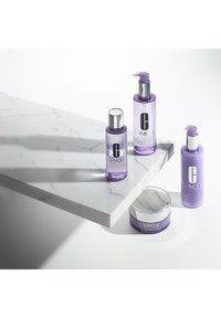 Trois produits de soin de la peau Clinique dans des bouteilles transparents violettes avec des accents argentés sur une surface en marbre blanc. Design propre et moderne avec un conteneur rond.