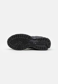 Semelle noire de chaussure de sport avec des crampons profonds et des motifs texturés, conçue pour l’adhérence et la durabilité sur différentes surfaces.