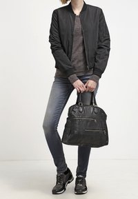 Svart bomberjacka, grå tröja och blå jeans. Håller en svart läderväska med flera dragkedjor. Svarta sneakers med vita sulor.