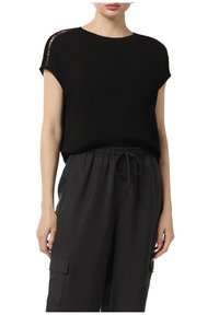 Black short-sleeve top with a loose fit, featuring cut-out details at the shoulders. Paired with gray elastic-waist cargo pants.