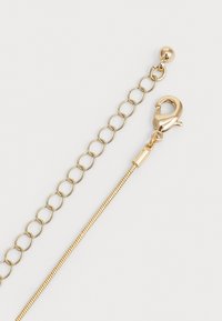 Goldene Kettenverlängerung mit Karabinerverschluss und kleiner runder Abschlussperle auf einem schlichten weißen Hintergrund.