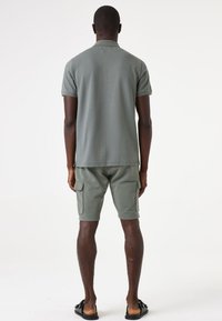 Lichtgroene polo met korte mouwen met een textuurpatroon, gecombineerd met bijpassende cargoshorts en sandalen, gezien vanuit de rug.