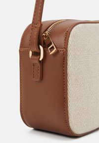 Borsa in finta pelle marrone con un pannello a spina di pesce in crema a trama, cerniera dorata e attacchi per la tracolla. Forma rettangolare, texture liscia e tessuta.