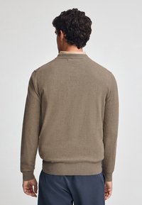 Maglione a maglia marrone con scollo a giro, polsini e orlo a coste, e una texture liscia. La vista posteriore mostra una silhouette aderente.