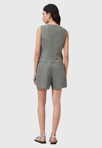 Top senza maniche in lino grigio abbinato a pantaloni corti a vita alta dello stesso colore. Presenta una silhouette aderente e cerniere sul retro. Indossato con sandali con cinghie.