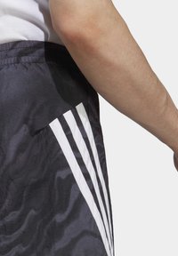 Pantaloni corti neri con strisce verticali bianche, realizzati in un tessuto leggero e morbido con una leggera texture stropicciata. Vita elastica visibile.