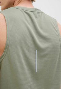T-shirt de sport sans manches en vert olive clair, fabriqué en tissu texturé. Présente un accent vertical blanc dans le dos pour un détail de design.