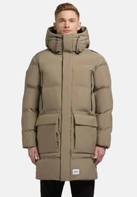 Giacca puffer beige con colletto alto, tasche a zip sul petto, due tasche anteriori con pattina e una silhouette lunga. Tessuto liscio e isolato.