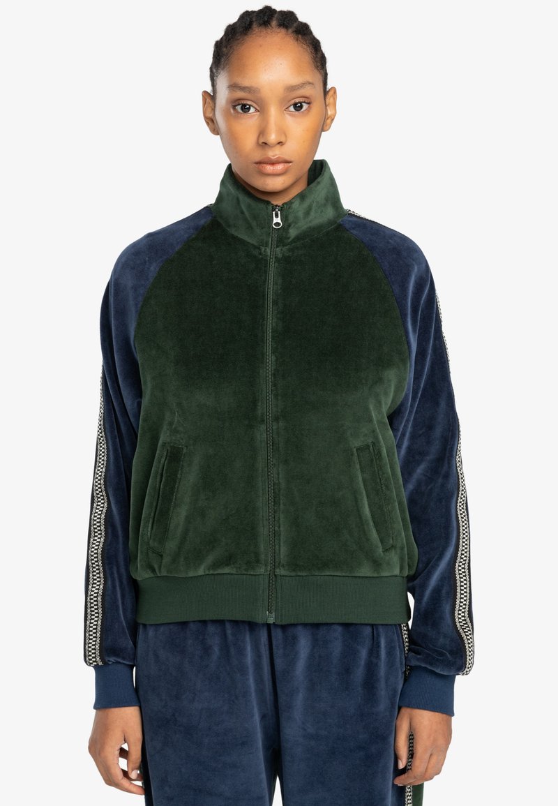 Chaqueta de felpa verde y azul marino con cremallera, bolsillos laterales, puños acanalados y acentos a rayas contrastantes a lo largo de las mangas.