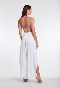 Achteraanzicht van een model dat een gestippelde roze en rode bralette draagt en een luchtige, witte wijde broek met een split en lichte textuur. Beige hakken.