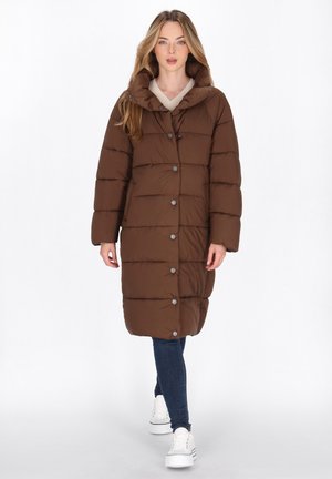 Brown padded coat with a high collar, snap buttons, and a long cut. Paired with blue jeans and white sneakers, featuring a smooth texture.