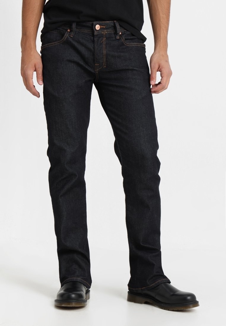 Mørkeblå denimjeans med slim fit, der har orange syninger, lukning med knapper foran og bæltestropper. Bruges med sorte sko.