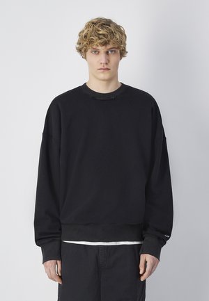 Sudadera negra con cuello redondo, hombros caídos y puños acanalados. La tela parece suave con una ligera textura. Diseño minimalista.