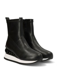 Botas de cuero negras hasta el tobillo con cierre de cremallera, punta redonda y suela blanca con un diseño de cadena negra en el talón.