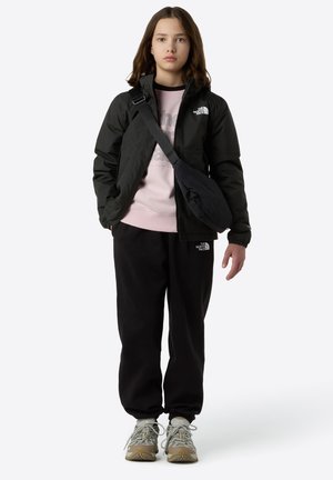 Schwarze wasserdichte Jacke, hellrosa Sweatshirt, schwarze Hosen, graue Sneaker mit gelben Akzenten und eine schwarze Umhängetasche. Lässige Outdoor-Bekleidung.