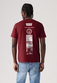 Burgundy színű pamut póló, amelynek hátoldalán grafikai tervezés található, rajta a "Levi's" logó, egy kör alakú emblémával és négy fényképes panellel.