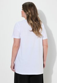 Camiseta blanca de manga corta, de corte relajado, con un escote redondeado y una textura suave. La longitud se extiende más allá de las caderas.