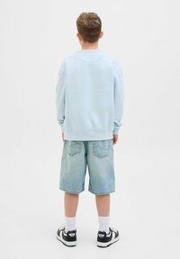 Felpa azzurra chiara con collo rotondo, abbinata a pantaloni corte in denim chiaro. L'outfit include calze bianche e sneakers nere con accenti bianchi.