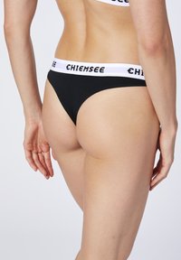 Schwarzer String mit einem weißen Bündchen, auf dem der Text "CHIEMSEE" steht. Der Stoff wirkt glatt und hat ein dehnbares Design für mehr Komfort.