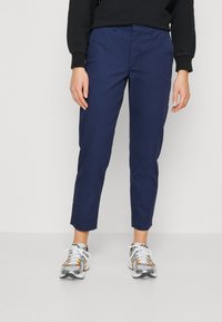 Pantaloni cropped blu navy, con una texture liscia e una leggera lucentezza. Presentano tasche anteriori e un design della cintura classico. Indossati con sneakers.