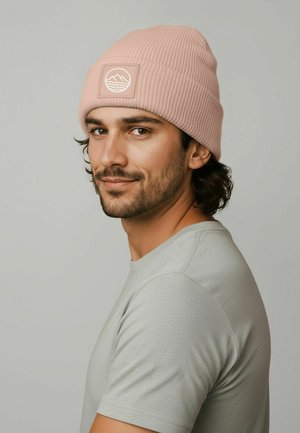 Pink ribbed knit beanie with a logo patch featuring waves, worn with a light gray t-shirt. The fabric appears soft with a textured finish.