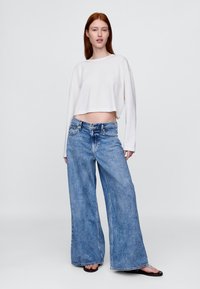 Bela majica z dolgimi rokavi, prirejena v kroju, združena z visokim pasom in širokimi svetlo modrimi kavbojkami iz jeansa. Gladek tekstura in klasični jeansa poudarki.