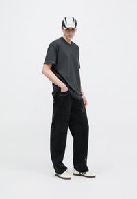 Szürke, túlméretezett rövid ujjú póló, fekete, szegecses részletekkel díszített kopott farmernadrág és csíkos, szürke-fehér sapka.