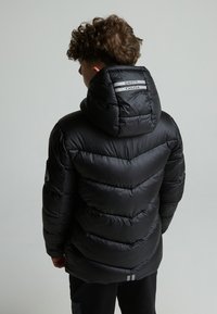 Doudoune noire avec capuche, présentant un motif en chevrons matelassés, une accentuation à rayures doubles à l'arrière et un patch logo sur le bras gauche.