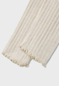 Les chauffe-jambes en tricot couleur crème présentent une texture côtelée avec de petits points en relief, ornés d'un ourlet froncé le long des bords.