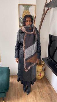 Must rohkem must nahast fliisiga jakk, millel on tekstureeritud viimistlus, tumedast hallist, pruunist ja heledast hallist villane sall, millel on sooniline äär, kantud musta seeliku peal.