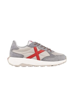 Sneaker grigia e beige con dettaglio rosso a forma di X sul lato, suola bianca e chiusura con lacci, vista dal lato esterno.