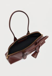 Καφέ δερμάτινη τσάντα με λεία υφή, χρυστό φερμουάρ και ευρύχωρο μαύρο εσωτερικό. Διαθέτει δύο λαβές και αποσπώμενο ταμπελάκι με το όνομα της μάρκας.