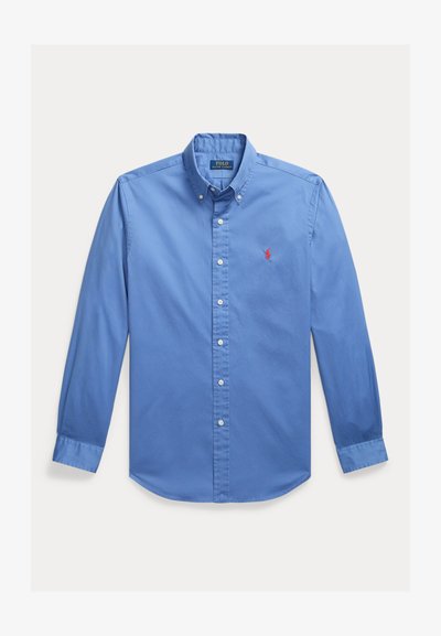 Chemise bleue à manches longues avec col boutonné, boutons blancs et petit logo rouge brodé sur la poitrine gauche.
