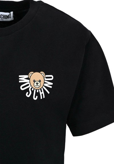 T-shirt en coton noir avec un graphique d'ours aux accents beige et blanc et le texte "MOSCHINO" en lettres stylisées et en gras.