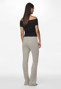 Svart av-skulder topp med ribbet tekstur, kombinert med beige flared bukser med vertikale svarte striper, begge tilpasset og uformelle.