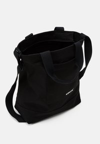 Tote bag en toile noire à la forme structurée, dotée de deux courtes poignées, d'une longue bandoulière réglable et d'une poche zippée intérieure.