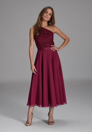 Burgundy evening dress with a one-shoulder lace bodice, flowing chiffon skirt, and gold heeled sandals. Smooth texture and elegant design.